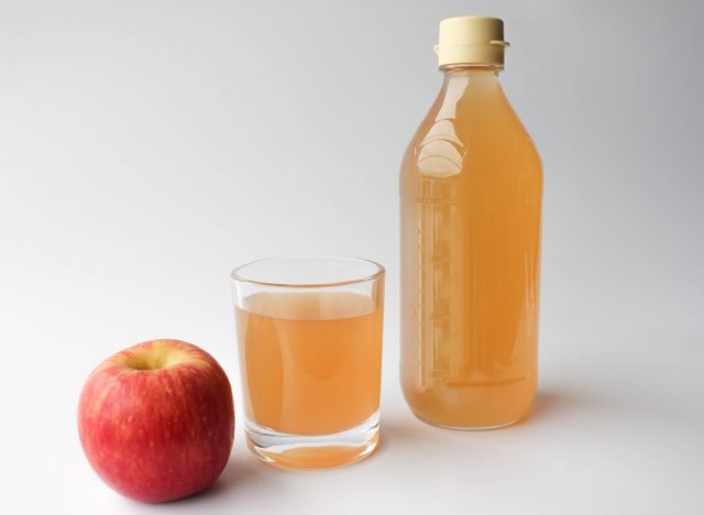 vinaigre de cidre de pomme dans une bouteille et un verre à côté d'une pomme