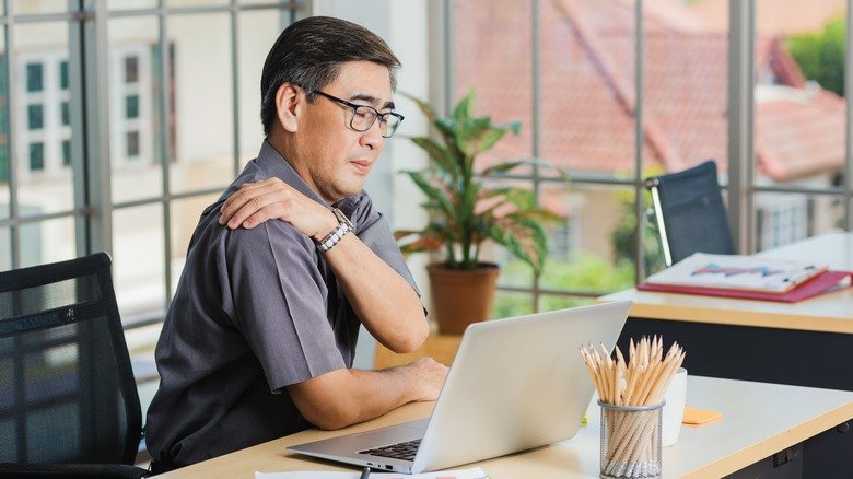 homme âgé souffrant de douleurs à l'épaule alors qu'il travaille à un bureau