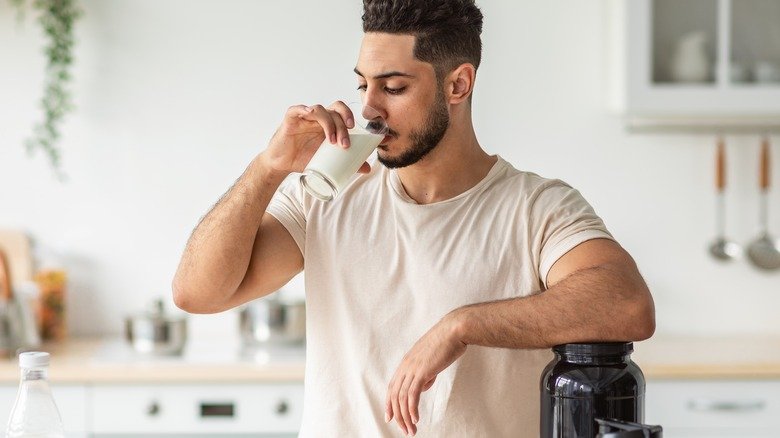 homme buvant un shake protéiné à côté d'un pot de poudre protéinée