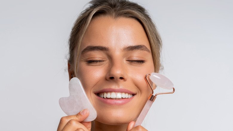 femme souriante alors qu'elle tient deux outils gua sha près de son visage