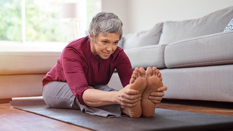 femme âgée assise sur un tapis d'exercice tenant ses orteils