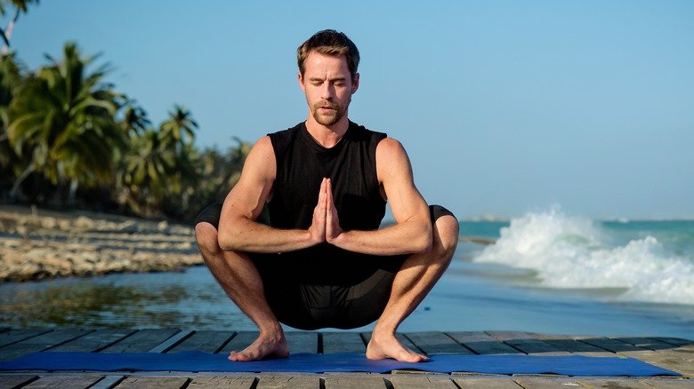 homme pratiquant le yoga squat sur une plage