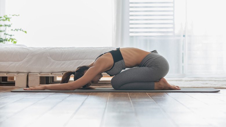 Femme faisant la posture de l'enfant à côté d'un lit 