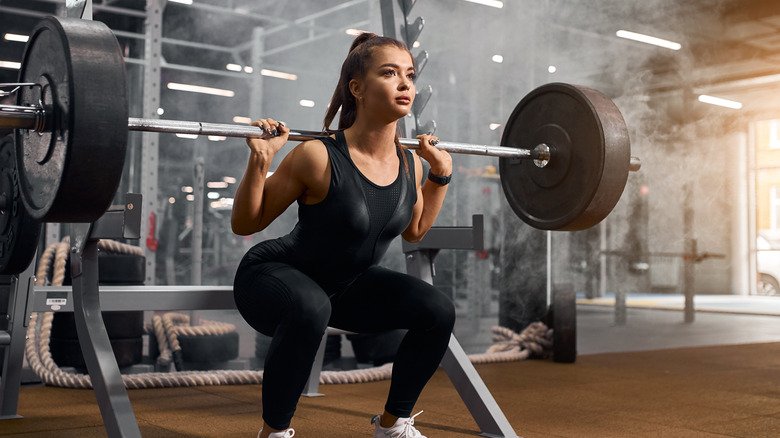 jeune femme effectuant des squats avec une barre lourde