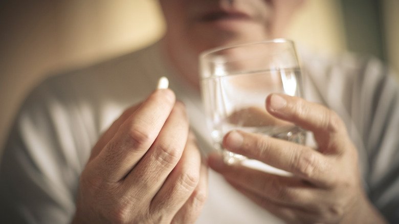 les mains d'un homme âgé tenant de l'eau et des médicaments