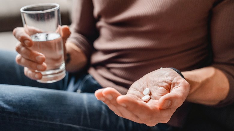 mains d'une femme tenant des médicaments et un verre d'eau