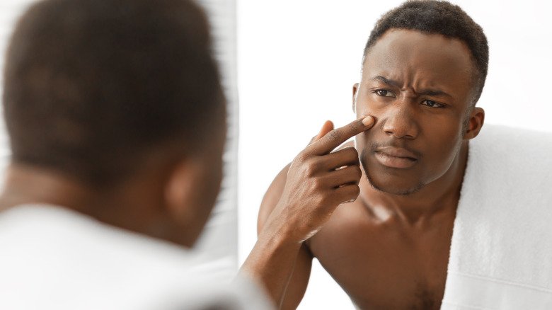 homme regardant l'acné dans le miroir