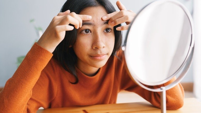 femme regardant son acné dans le miroir