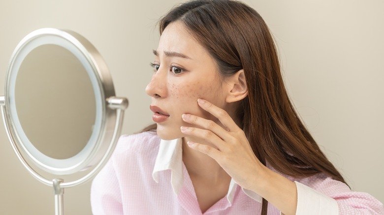 femme regardant l'acné dans le miroir