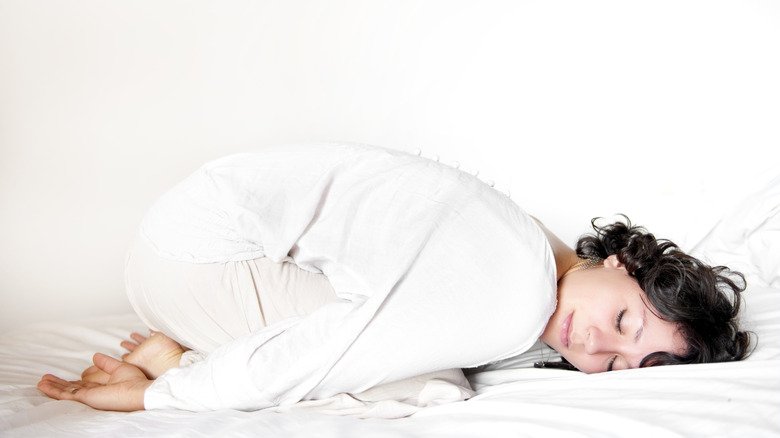 Une femme fait la posture de l'enfant au lit, les yeux fermés