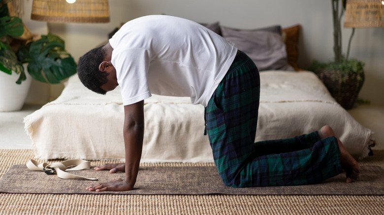 Un homme faisant la posture du chat sur un tapis de yoga devant un lit