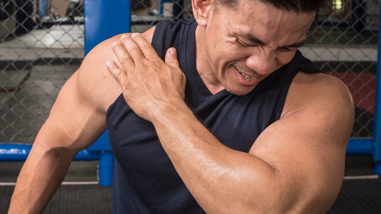 un homme dans la salle de sport se tient l'épaule de douleur