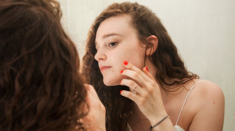 femme regardant l'acné dans le miroir