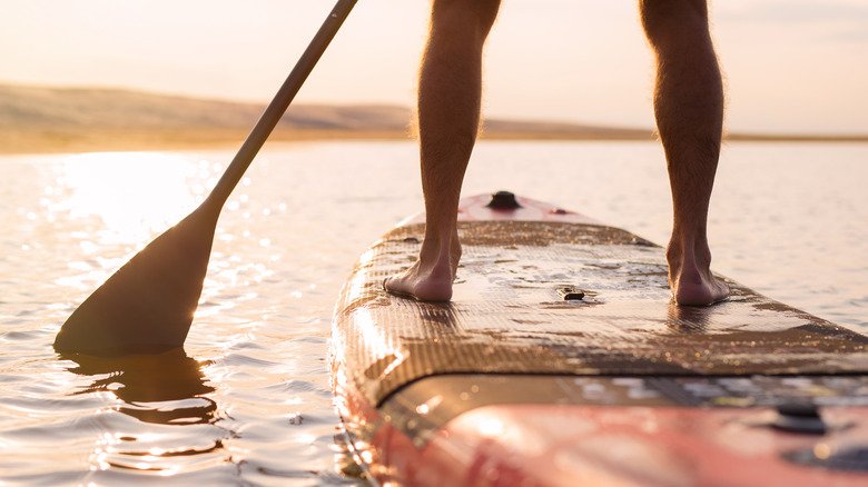 jambes d'un homme sur un paddleboard au coucher du soleil