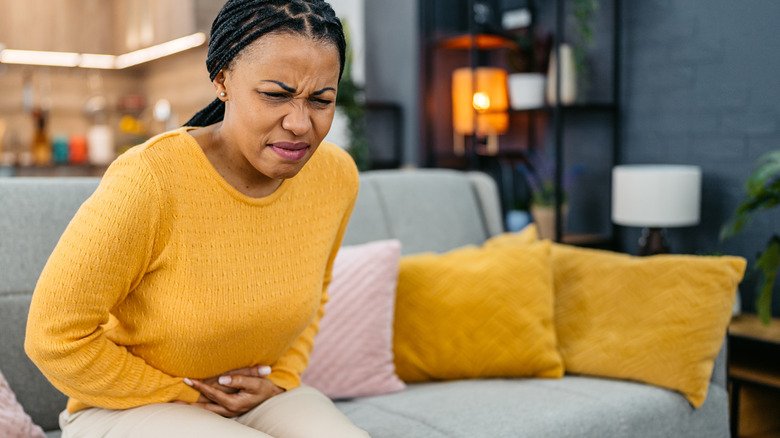 femme assise sur un canapé se tenant le ventre en signe d'inconfort