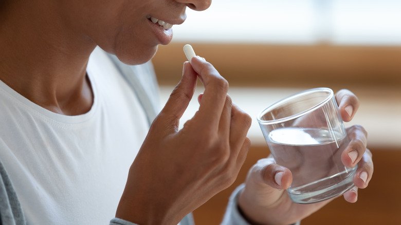 Femme tenant un verre d'eau et prenant une pilule