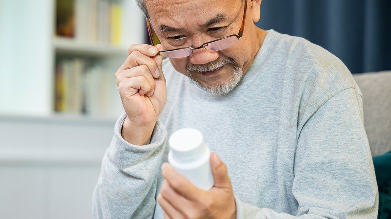 Un homme avec des lunettes lit une étiquette de médicament