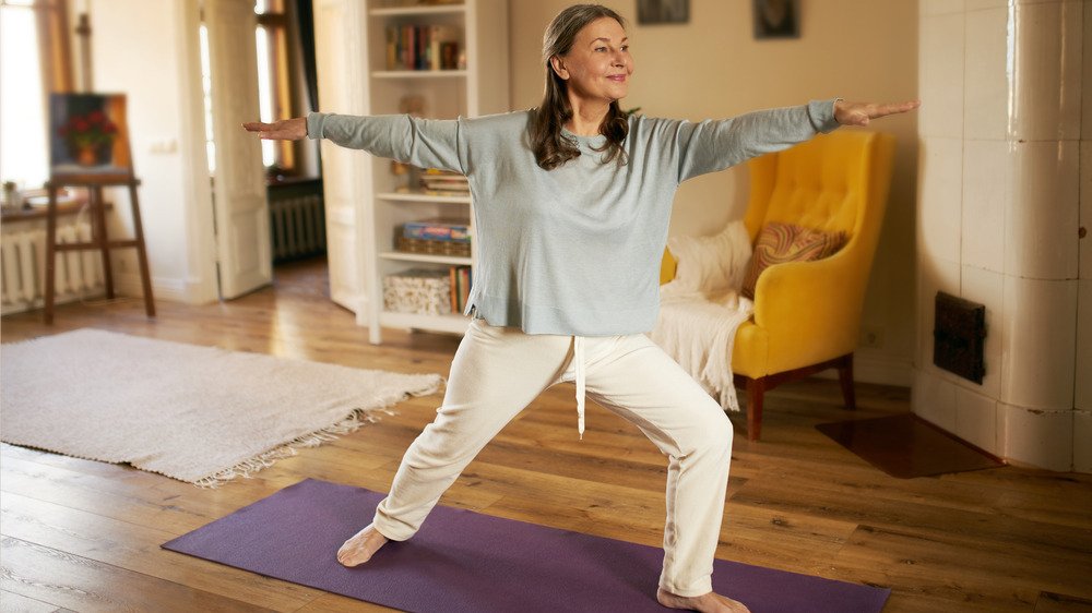 Femme âgée pratiquant le yoga sur un tapis à la maison