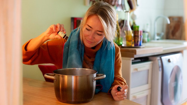 femme mettant de l'huile essentielle dans une casserole d'eau bouillie