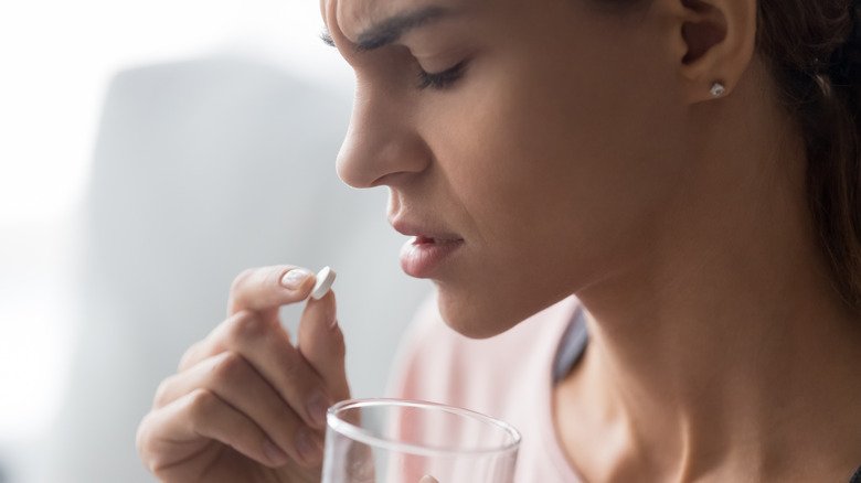 Une femme hésite à prendre un comprimé d'ibuprofène