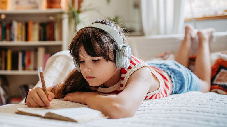 fille allongée sur le lit écoutant de la musique et tenant un journal