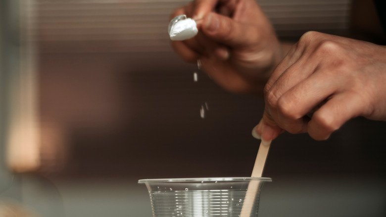 main d'une femme versant du bicarbonate de soude dans un verre d'eau