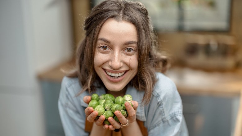 femme souriante tenant une poignée de choux de Bruxelles