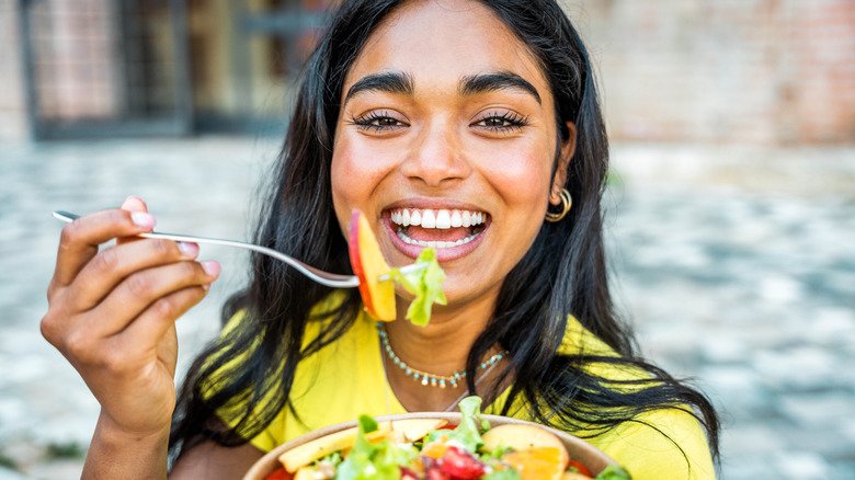 femme souriante mangeant un bol de fruits et légumes