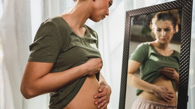 femme regardant son ventre gonflé dans le miroir