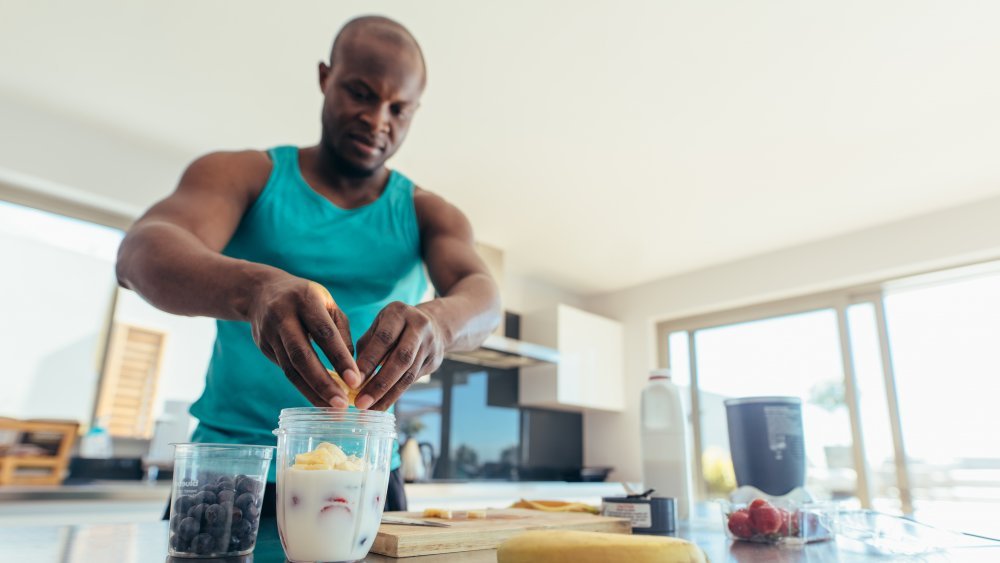 Un homme prépare un milk-shake dans la cuisine. Un homme athlétique ajoute des fruits à un pot de lait. Régime inversé.