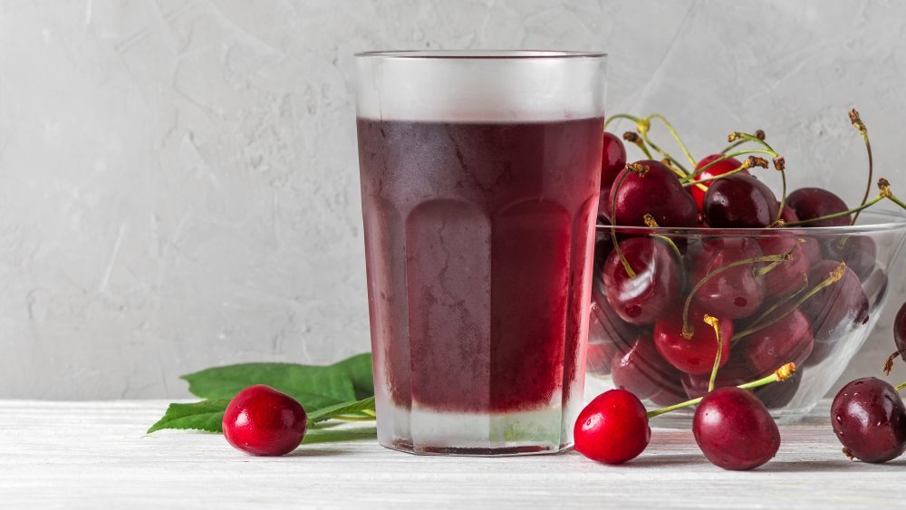 Un verre de jus de cerise avec un bol de cerises à côté 