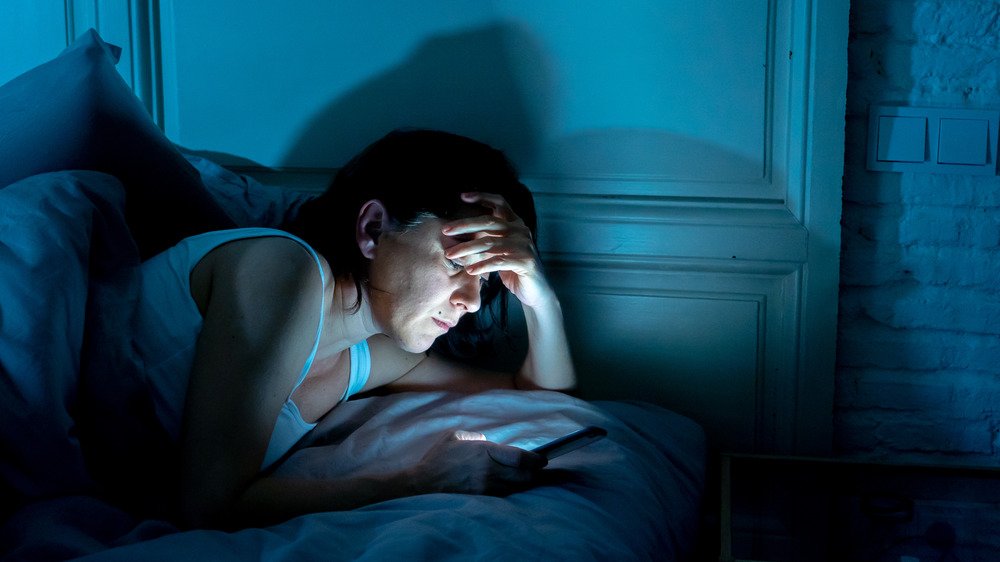 Une femme regarde son smartphone au lit