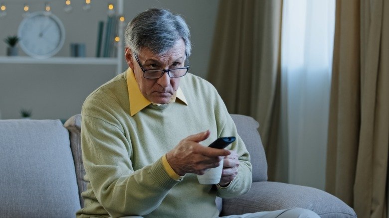 Homme assis sur un canapé tenant une télécommande