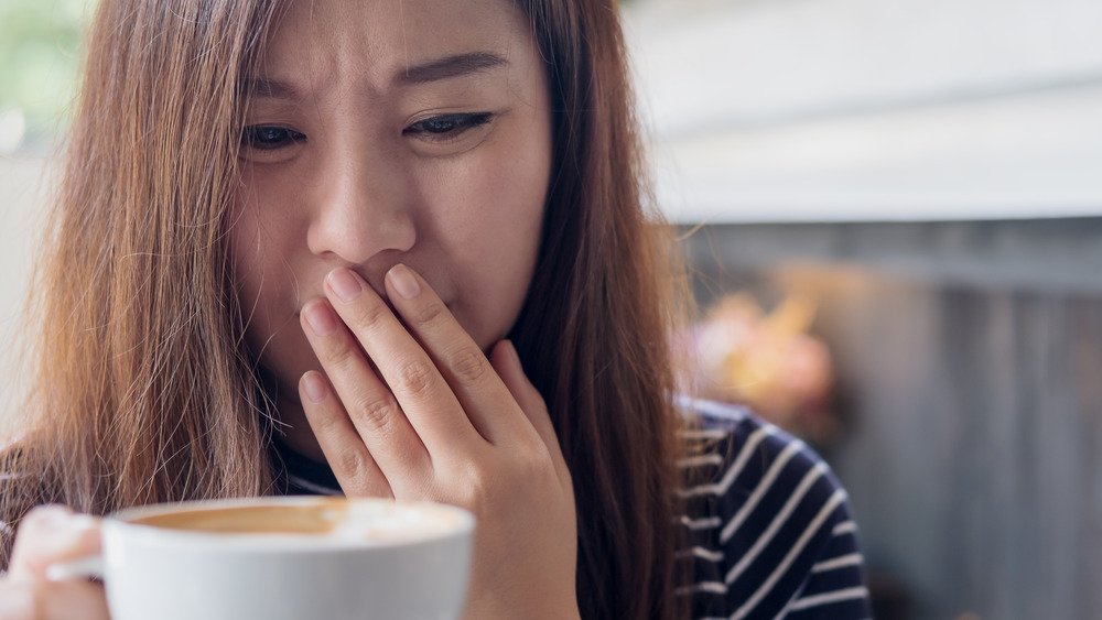 Une femme tenant une tasse de café avec un air déconcerté 