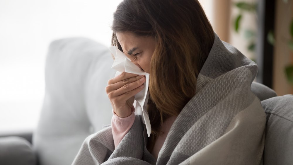 Femme malade dans une couverture avec des mouchoirs sur un canapé