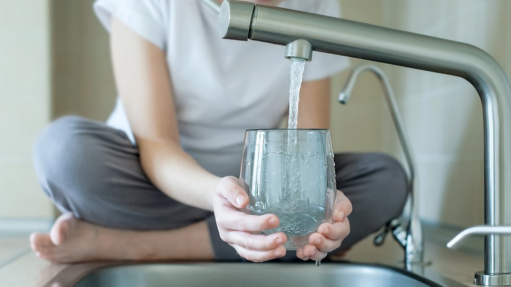 Un enfant remplit un verre d'eau de l'évier de la cuisine 