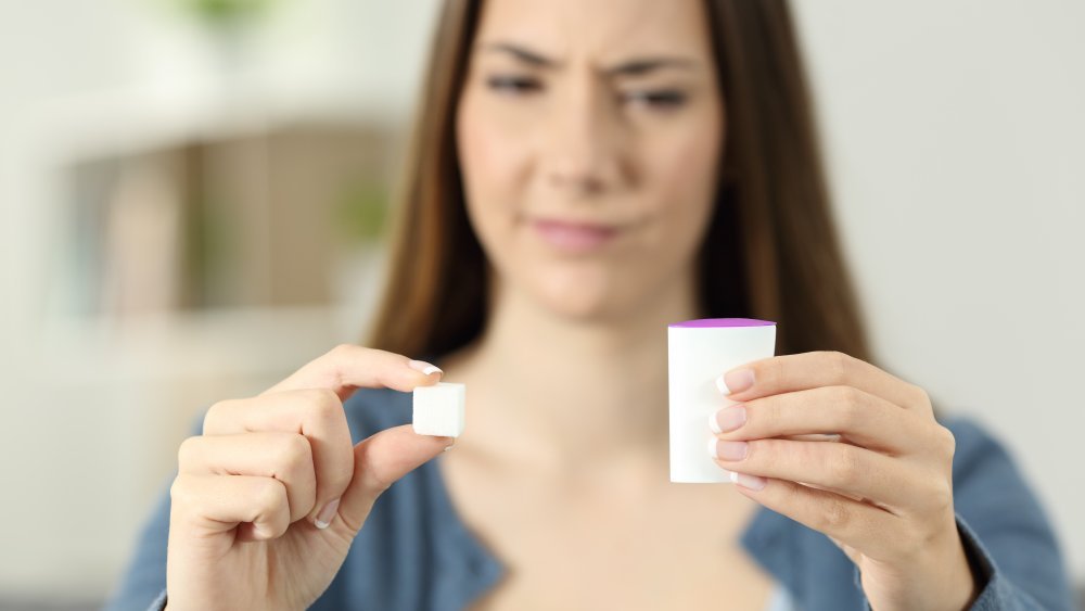 Une femme confuse hésitant entre la saccharine et le sucre à la maison