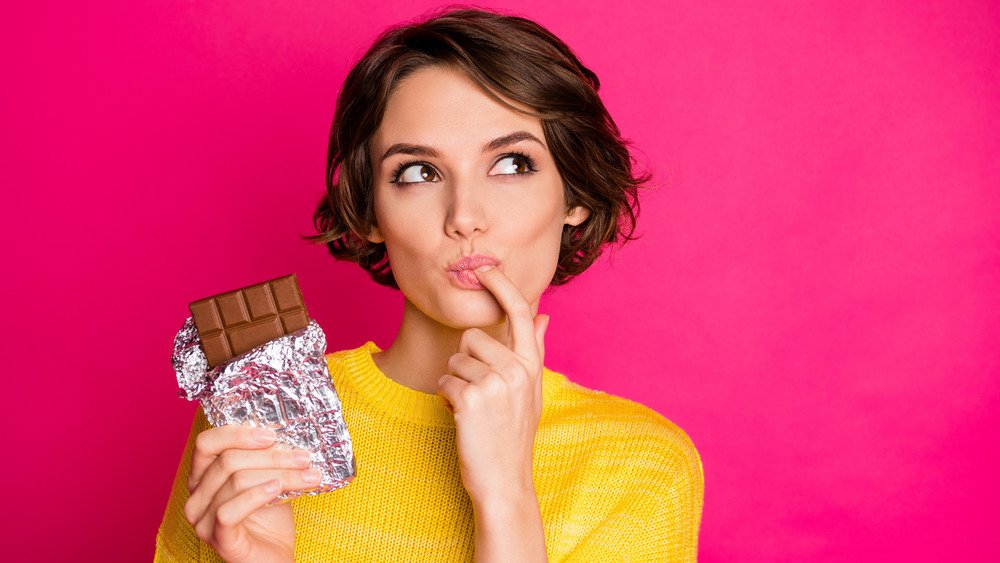 Jeunes femmes en pull jaune tenant une barre de chocolat noir