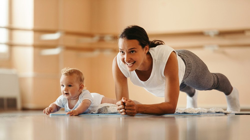 Une mère sportive s'exerce en position de planche tout en étant avec son bébé