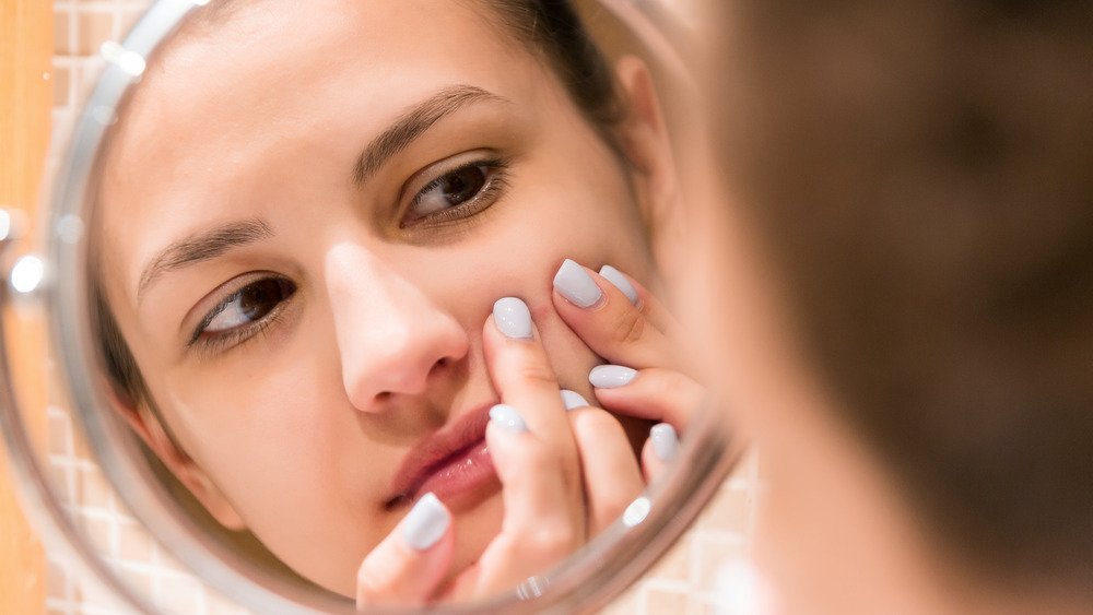 Une jeune femme serre un bouton sur son visage en se regardant dans le miroir