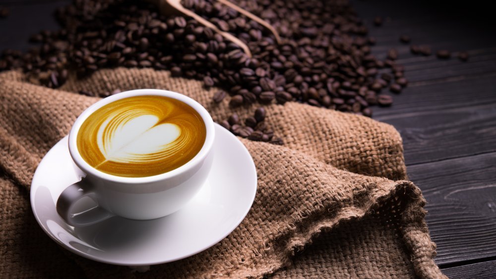 Tasse de café au lait en forme de cœur et grains de café sur fond de bois ancien