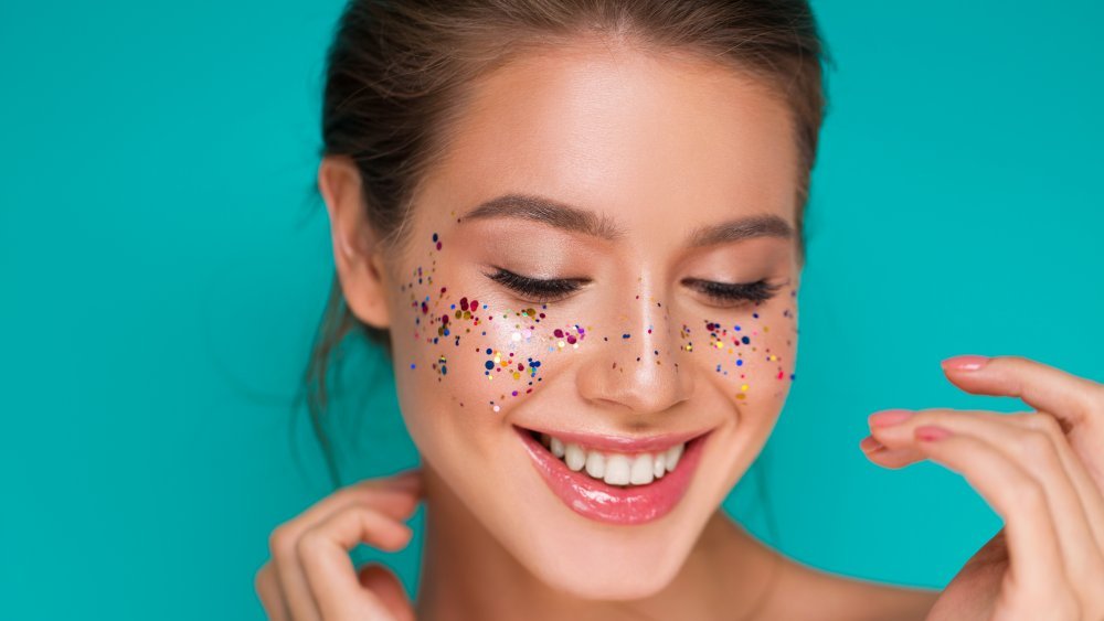 Femme avec des paillettes sur ses joues rougissant sur fond bleu vert