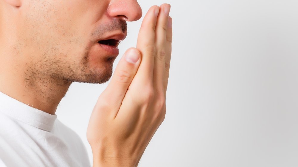 Un homme en chemise blanche vérifie sa respiration avec sa main