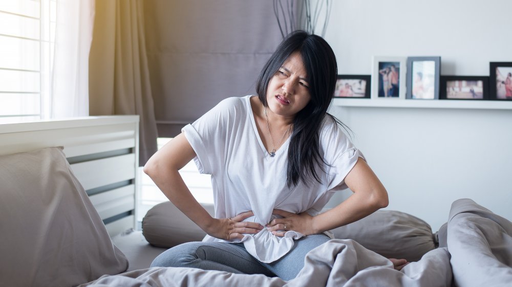 Femme assise sur le lit tenant son abdomen