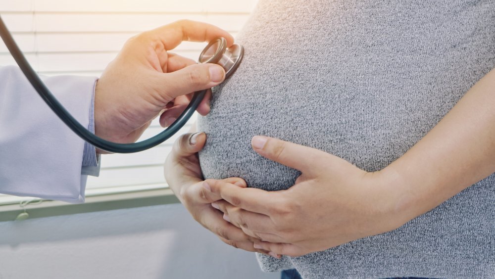 Un médecin avec un stéthoscope écoute le ventre d'une femme enceinte