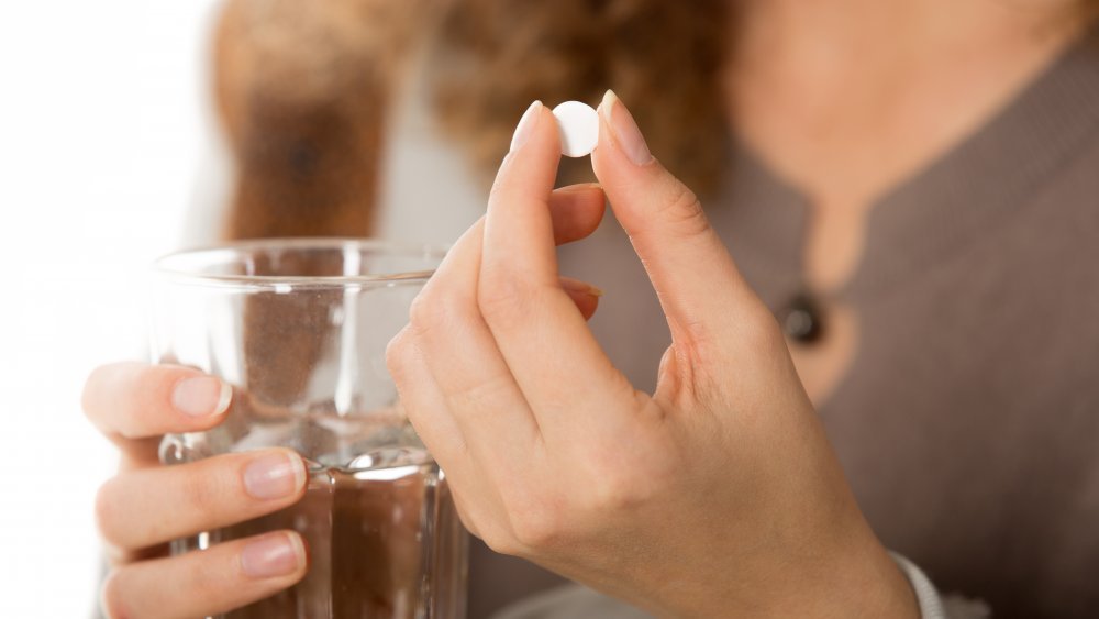 Une photo en gros plan de mains de femmes tenant une pilule ronde blanche et un verre d'eau