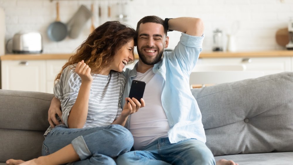 Couple homme-femme se câlinant sur le canapé en regardant le téléphone