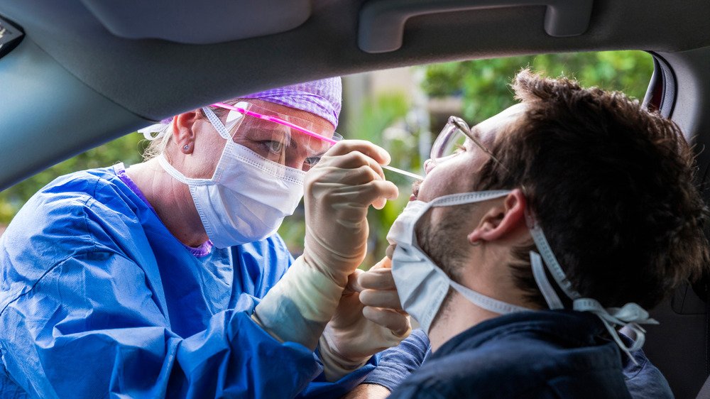 Un professionnel de la santé effectue un test par écouvillonnage nasal sur un patient dans une voiture