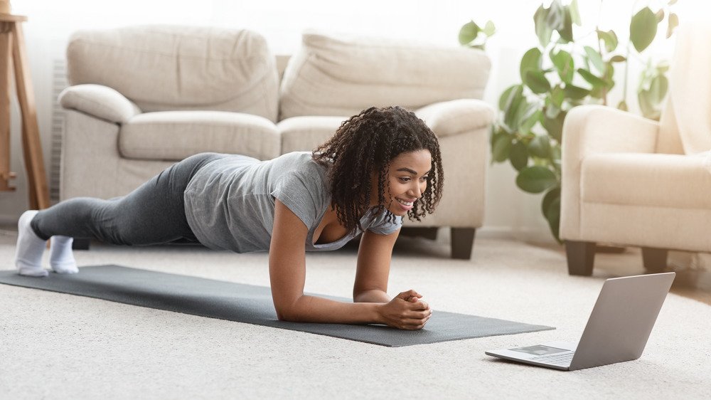 Femme noire en forme faisant du yoga en planche tout en regardant un tutoriel en ligne sur un ordinateur portable