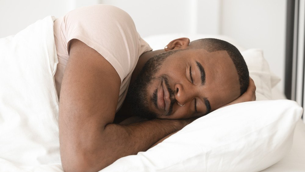 Un jeune homme noir serein et calme dort bien seul sur un oreiller orthopédique doux sous une couette chaude, un homme afro-américain endormi dans un lit confortable et douillet profite d'une bonne nuit de sommeil paisible et sain